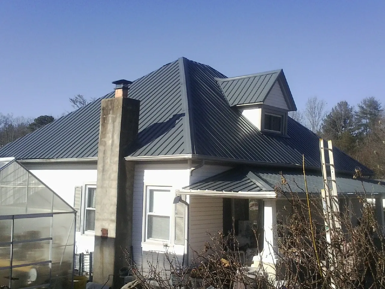 Dark blue standing seam metal roof on a white farmhouse with dormer — Slate & Tile Roof Repair by Roofing Brothers in La Follette