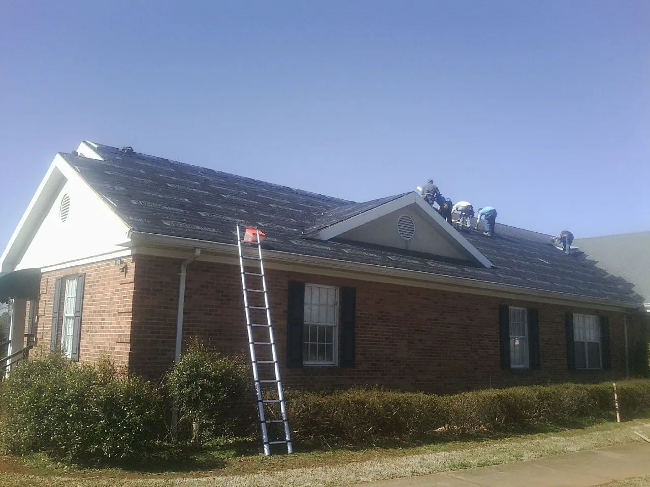 Crew tearing shingles off a brick ranch roof with a ladder set — Emergency Roof Repair work by our crew in La Follette