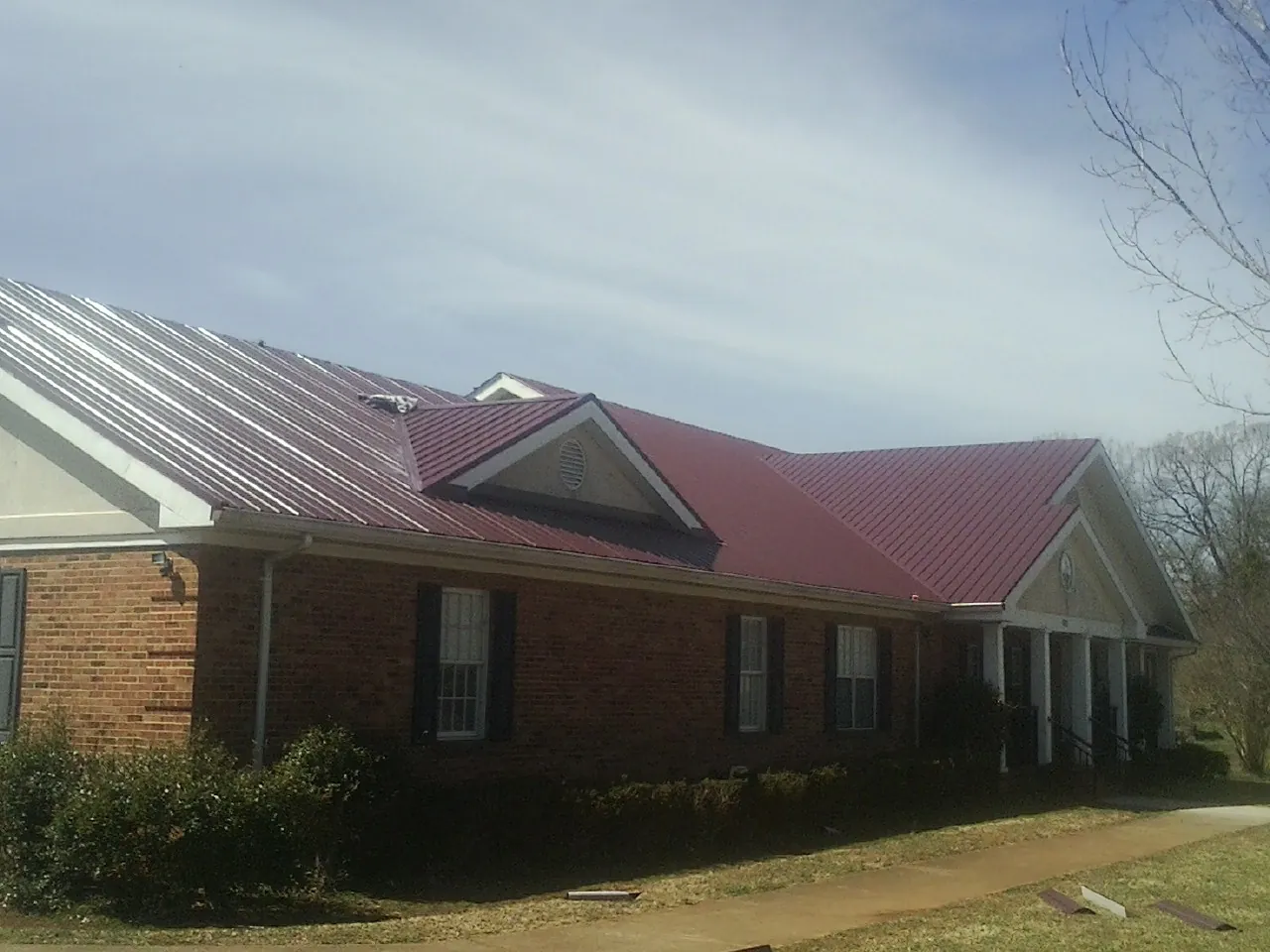 Red metal roof with gabled entries on a long brick building, from a Hail Damage Roof Repair job in La Follette
