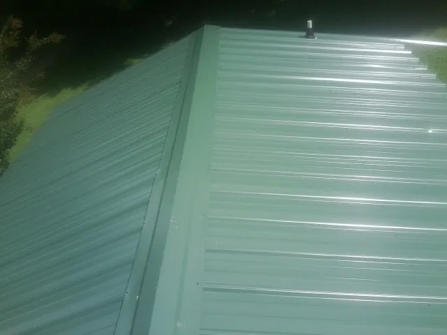 New green metal panels meeting at the ridge of a roof — Flat Roof Repair work by our crew in La Follette