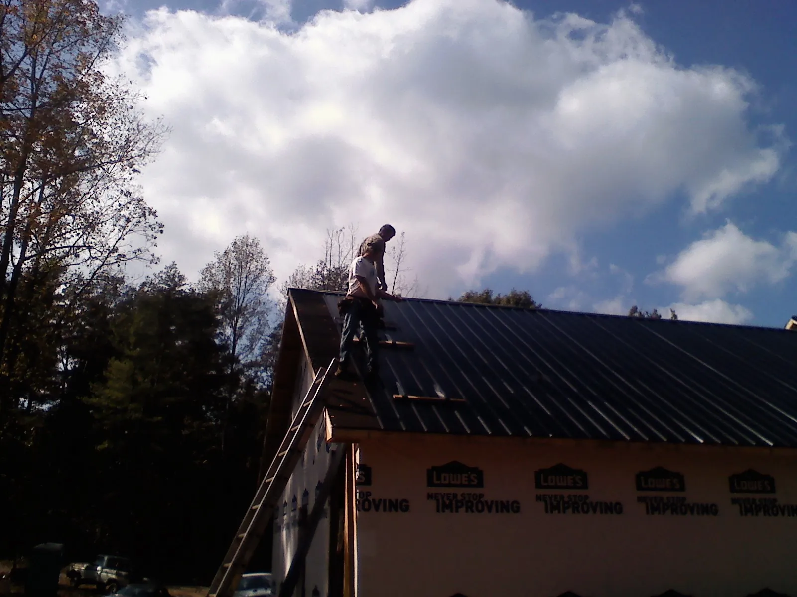 Roofer fastening dark metal panels high against a cloudy sky, from a Roof Inspection job in La Follette