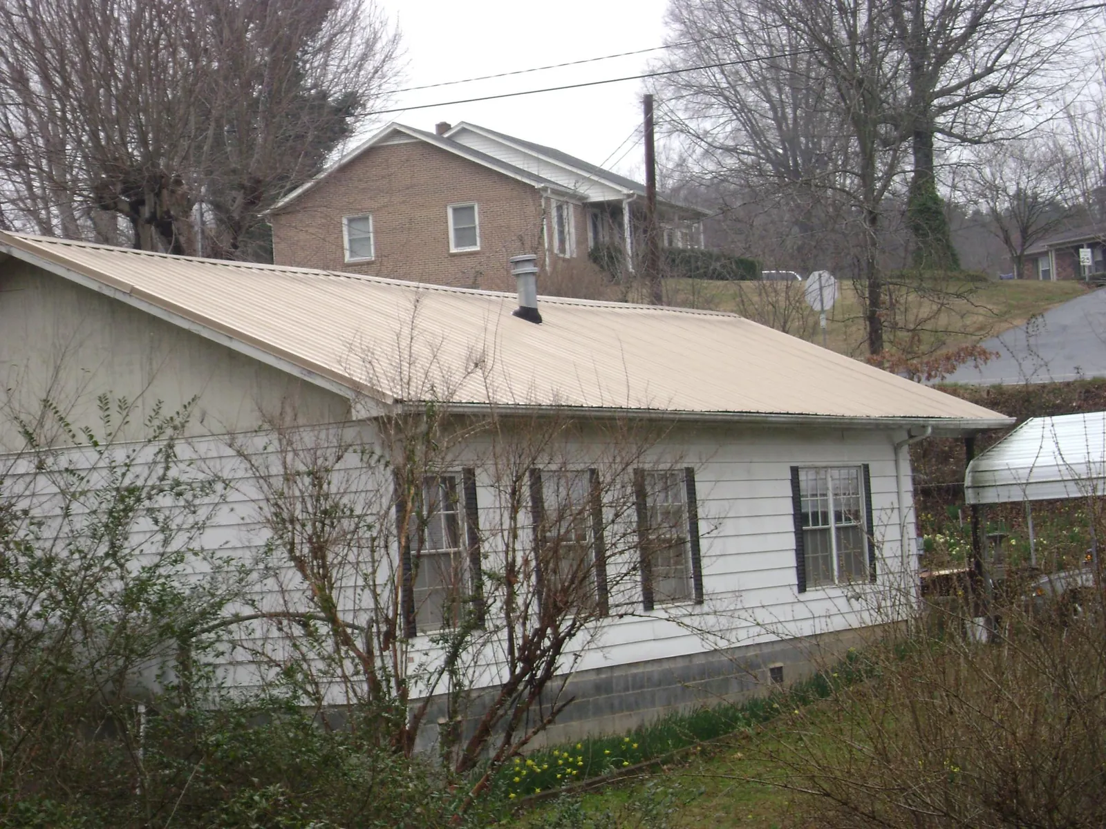 Tan metal roof on a white sided house set into a hillside — Commercial Roofing by Roofing Brothers in La Follette